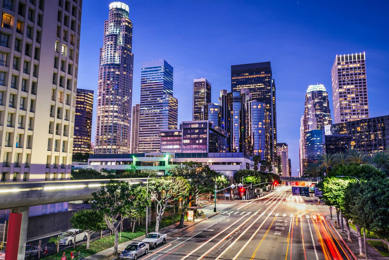 Downtown Los Angeles, California at dusk, with illuminated skyscrapers and light trails from traffic on city streets.